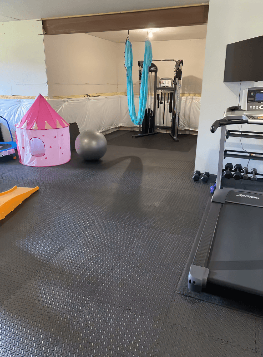 Home gym with black interlocking EVA foam mats, including treadmill and exercise equipment, ensuring a non-slip workout surface.